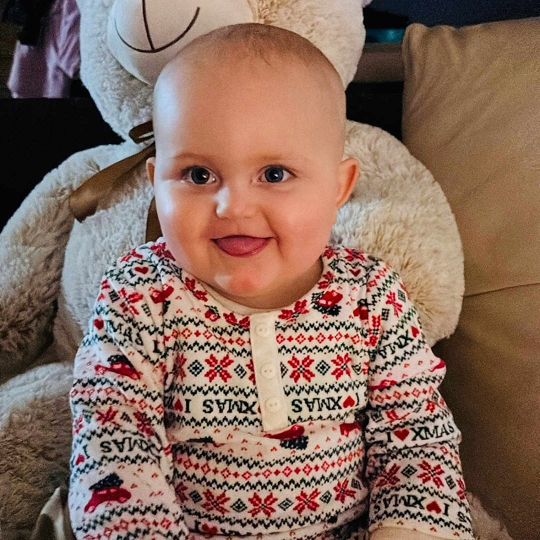 Giulia participe au concours pour gagner de l'argent avec cette photo : baby, blanket, child, couch, cozy, cute, face, festive_clothing, happy, holiday, home, indoor, pajamas, person, plush_toy, seated, smile, soft_toy, teddy_bear, tongue_out