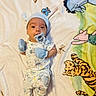 baby, infant, pajamas, mittens, pacifier, hat, blanket, animal_print, tiger, elephant, pig, dragonfly, striped_socks, lying_down, cute, child, indoors, soft_texture, colorful, portrait