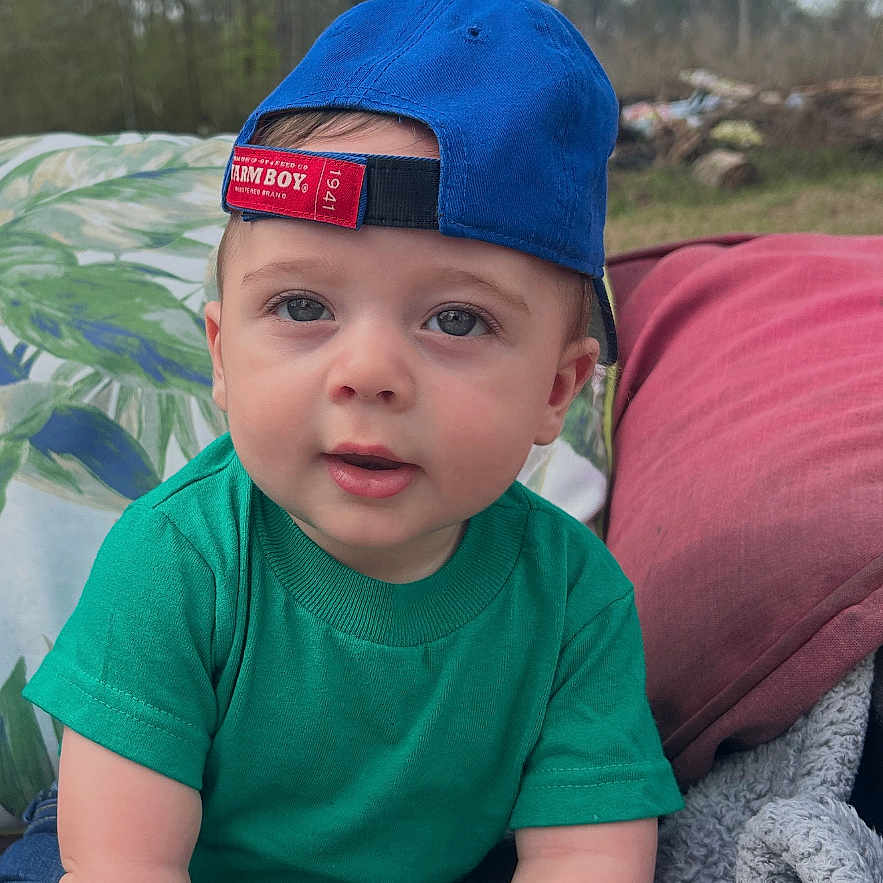 Clay joined the competition — help win amazing prizes! baby, blanket, blue_cap, casual_clothing, child, curious, cute, daylight, expression, grass, green_shirt, headwear, nature, outdoor, portrait, sitting, sky, toddler, trees, young_child