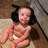 Clay is registered to the contest to win money with this photo: baby, carpet, cheeks, child, couch, cute, diaper, earmuffs, expression, floor, furniture, home, indoor, infant, person, playful, sitting, skin, tongue_out, wooden_floor