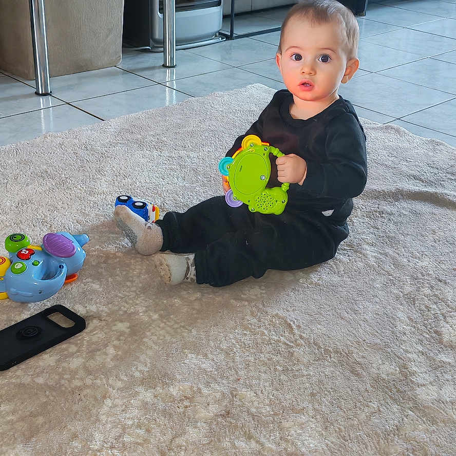 Jérémy a rejoint le concours — aidez-le/la à gagner de superbes lots ! black_clothing, cabinet, child, colorful_toy, curious, expression, floor_tiles, furniture, home, indoor, living_room, person, plant, playful, rug, sitting, television, toddler, toy, young_child