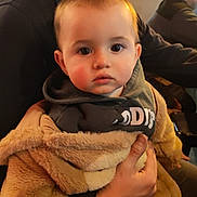 Jérémy a rejoint le concours — aidez-le/la à gagner de superbes lots ! toddler, child, baby, person, face, indoor, warm_lighting, jacket, hoodie, hand, adult, holding, seated, curious, expression, cozy, fuzzy, clothing, portrait, closeup