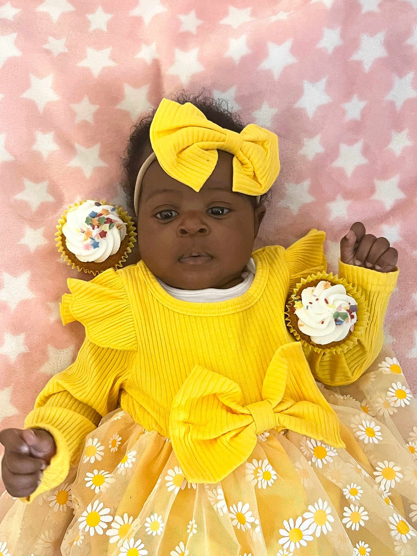 Omoize is registered to the contest to win money with this photo: baby, child, yellow_dress, bow, headband, cupcake, sprinkles, blanket, stars, pink_background, smiling, cute, infant, tutu_skirt, floral_pattern, celebration, sweet, happy, soft_texture, portrait