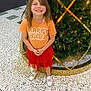 Kalina joined the competition — help win amazing prizes! child, smiling, girl, happy, standing, christmas_tree, holiday_decor, orange_shirt, red_skirt, white_sneakers, indoor, floor, lighting, festive, decorations, greenery, ribbons, face, person, portrait