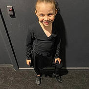 Kalina is registered to the contest to win money with this photo: child, girl, smile, dancewear, black_clothing, bow, hair_tied, pose, standing, indoor, carpeted_floor, wall, light_switch, happy, young, person, footwear, leggings, long_sleeves, portrait