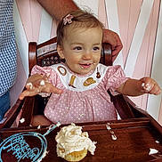 Sadie joined the competition — help win amazing prizes! toddler, child, cupcake, frosting, highchair, pink_dress, polka_dot, cream, smiling, happy, face, hands, arm, wood, chair, birthday, celebration, food, messy, indoor