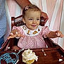 toddler, child, cupcake, frosting, highchair, pink_dress, polka_dot, cream, smiling, happy, face, hands, arm, wood, chair, birthday, celebration, food, messy, indoor