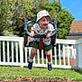 Jasper is registered to the contest to win money with this photo: toddler, child, swing, playground, hat, shorts, shirt, smiling, outdoor, daylight, greenery, fence, grass, shoes, white_socks, happy, fun, park, summer, leisure