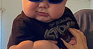 Gunnar joined the competition — help win amazing prizes! baby, child, infant, sunglasses, blue_glasses, portrait, being_held, adult_hands, indoor, home, close_up, face, cheeks, short_hair, dark_clothing, graphic_shirt, seated, candid, funny_expression, fashionable