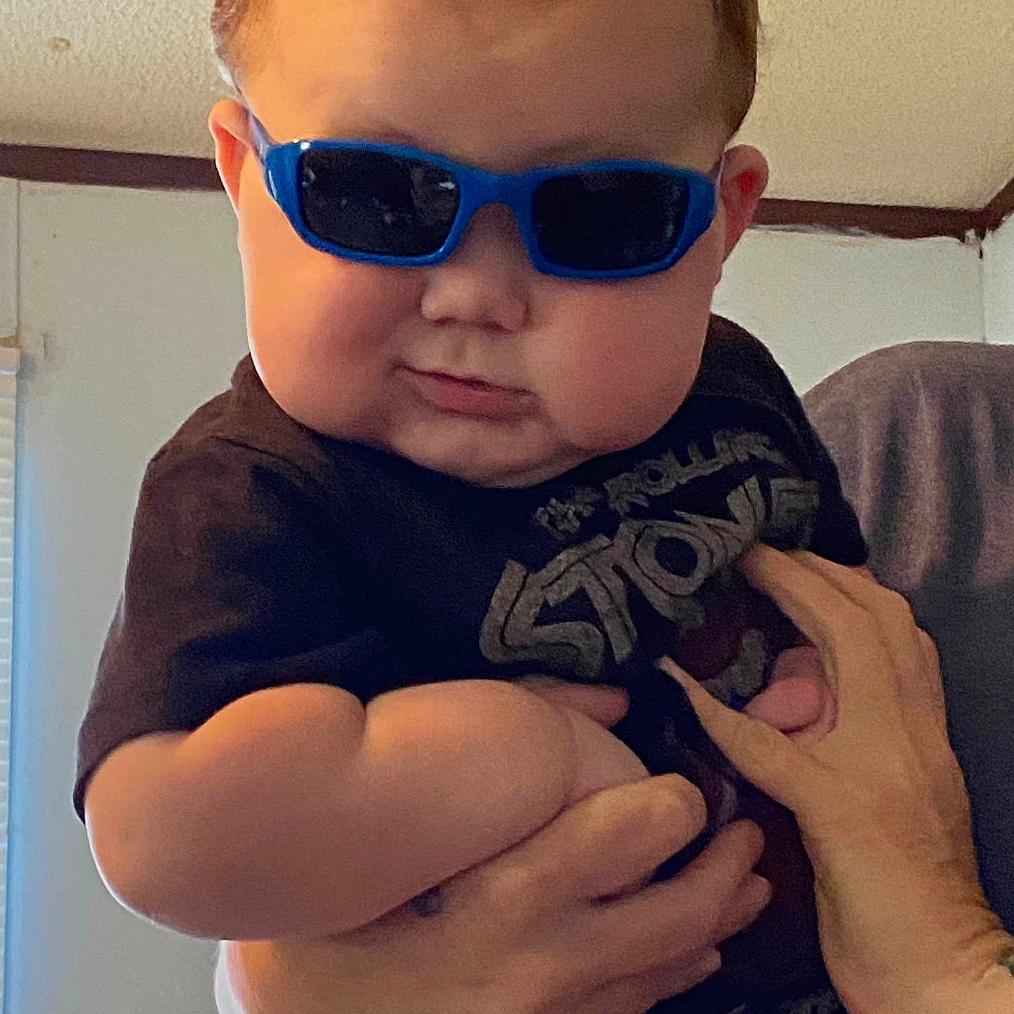 Gunnar joined the competition — help win amazing prizes! baby, child, infant, sunglasses, blue_glasses, portrait, being_held, adult_hands, indoor, home, close_up, face, cheeks, short_hair, dark_clothing, graphic_shirt, seated, candid, funny_expression, fashionable
