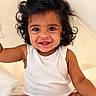 baby, child, smiling, curly_hair, white_onesie, sitting, portrait, cute, happy, infant, face, skin, arm, indoors, light_background, baby_toddler, person, young_child, expression, closeup