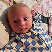 Harley joined the competition — help win amazing prizes! baby, infant, face, eyes, onesie, checkered_pattern, blue, cream, quilt, bed, soft_light, skin, arm, lying_down, curious, portrait, child, closeup, indoors, cute