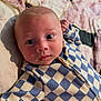 baby, infant, face, eyes, onesie, checkered_pattern, blue, cream, quilt, bed, soft_light, skin, arm, lying_down, curious, portrait, child, closeup, indoors, cute