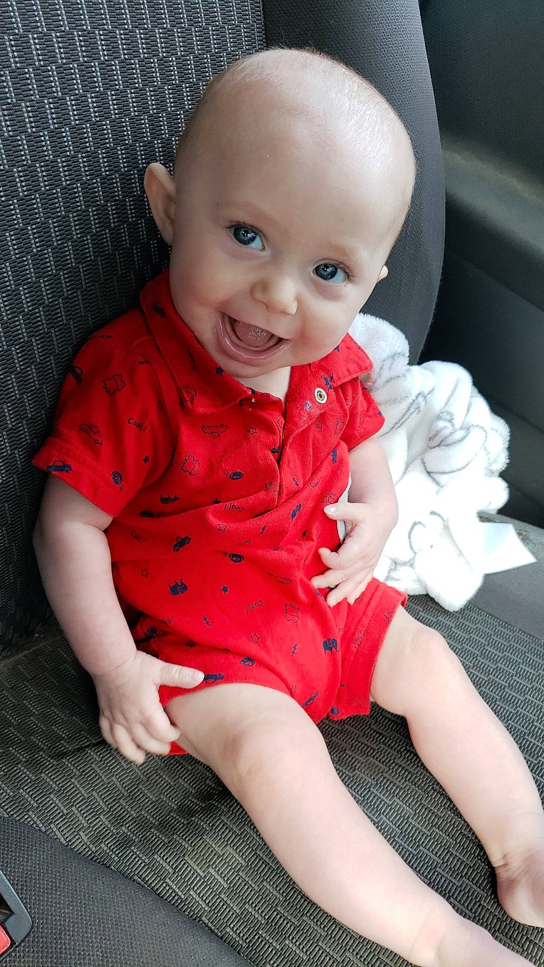 Grayson is registered to the contest to win money with this photo: baby, blanket, blue_eyes, car_seat, child, clothing, cute, face, hand, happy, indoor, infant, leg, portrait, red_clothing, seat, sitting, skin, smile, toe