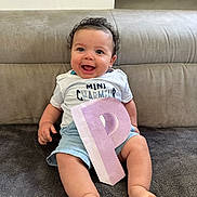 Kayden a rejoint le concours — aidez-le/la à gagner de superbes lots ! baby, child, smiling, curly_hair, white_shirt, blue_shorts, letter_p, pink_letter, sitting, blanket, couch, happy, indoors, portrait, cute, feet, hand, face, person, young_child