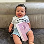 baby, child, smiling, curly_hair, white_shirt, blue_shorts, letter_p, pink_letter, sitting, blanket, couch, happy, indoors, portrait, cute, feet, hand, face, person, young_child