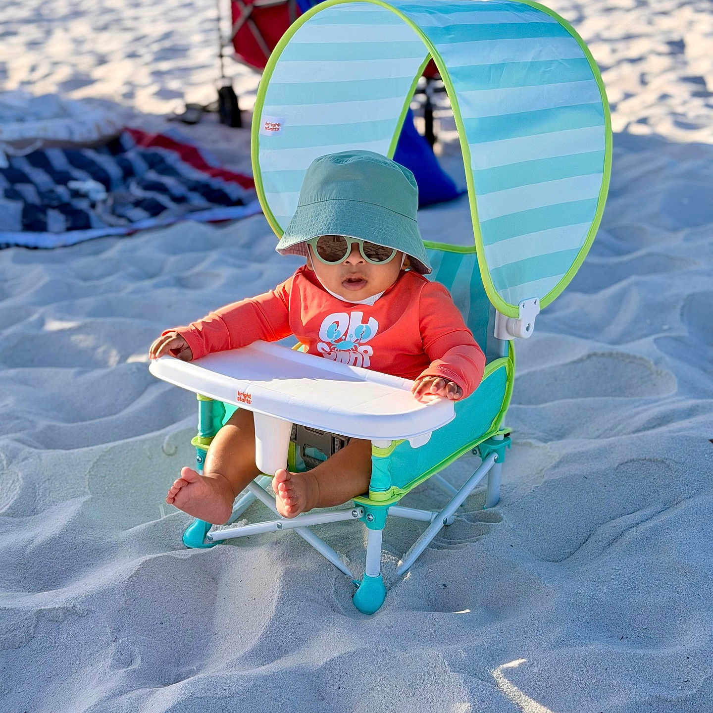 Adrian is registered to the contest to win money with this photo: baby, child, beach, sand, sunshade, hat, sunglasses, chair, outdoor, summer, sun_protection, footwear, infant, toy_cart, blanket, relaxation, sunny, vacation, casual_clothing, playtime
