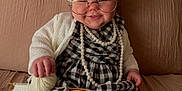Emory joined the competition — help win amazing prizes! baby, child, costume, glasses, knitting, yarn, wool, pearls, plaid_dress, couch, smile, indoors, cute, funny, handmade, white_hair_wig, knitting_needles, cozy, sitting, portrait