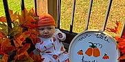 Luka joined the competition — help win amazing prizes! baby, infant, pumpkin, autumn_leaves, orange_hat, onesie, porch, wooden_floor, decorative_pumpkin, fall, seasonal_decor, sign, hand_painted, outdoor, green_grass, fence, baby_clothing, cute, sitting, holiday