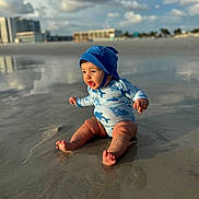Enzo is registered to the contest to win money with this photo: baby, child, beach, sand, water, swimsuit, hat, ocean, sunlight, clouds, reflection, sitting, smiling, outdoor, summer, vacation, nature, happy, toddler, play