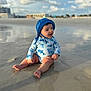 Enzo is registered to the contest to win money with this photo: baby, child, beach, sand, water, swimsuit, hat, blue, sunny, clouds, reflection, smiling, sitting, outdoor, happy, person, nature, daytime, shore, vacation
