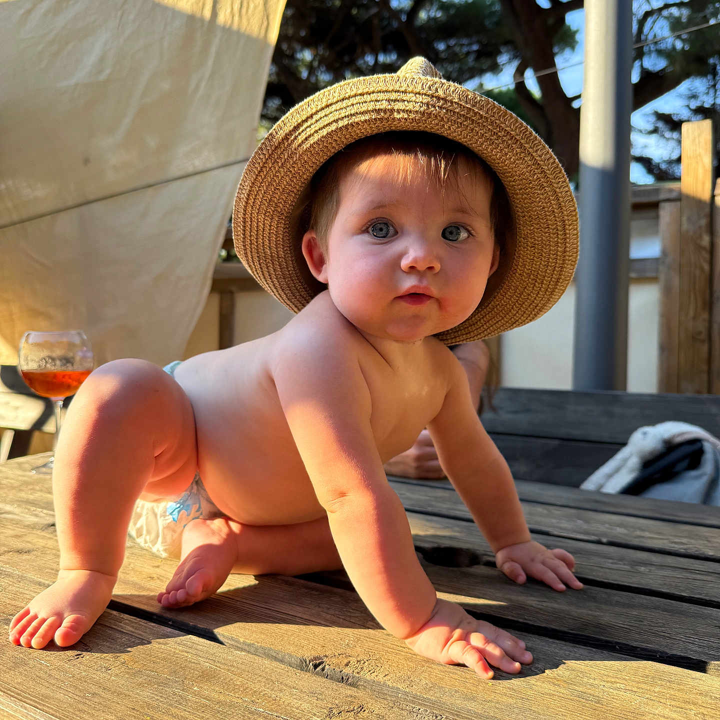 Castille participe au concours pour gagner de l'argent avec cette photo : baby, backyard, blue_eyes, child, crawling, curious, cute, daylight, diaper, face, hat, nature, outdoor, person, straw_hat, summer, sunlight, table, wood, wooden_table
