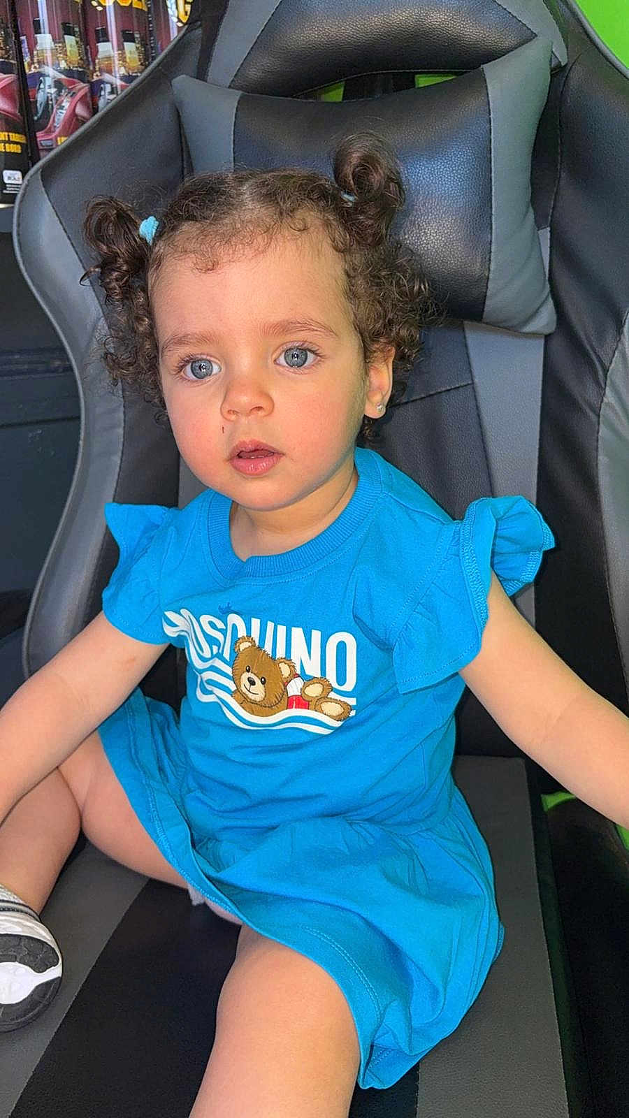 Chérine participe au concours pour gagner de l'argent avec cette photo : toddler, child, blue_dress, curly_hair, pigtails, gaming_chair, indoor, cute, portrait, sitting, face, eyes, expression, clothing, shoe, black, gray, young_child, innocent, casual