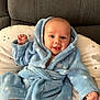 baby, infant, smile, blue_bathrobe, cozy, fist, pillow, couch, happy, face, head, child, clothing, indoor, soft_texture, cute, portrait, newborn, sitting, warm