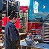 child, woman, fire_truck, vehicle, outdoor, daylight, person, face_paint, sneakers, jeans, jacket, reflection, metal, bumper, equipment, smile, side_view, casual_clothing, curly_hair, interaction