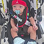 Dayden is registered to the contest to win money with this photo: baby, infant, pacifier, headband, car_seat, sneakers, white_shoes, blue_eyes, black_clothing, red_headband, bib, baby_bib, straps, sitting, cute, child, indoors, car_seat_pattern, footwear, young_child