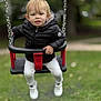 child, toddler, swing, playground, jacket, white_pants, white_shoes, outdoor, park, grass, metal_chains, black_jacket, happy, person, young_child, fun, play, casual_clothing, daytime, nature