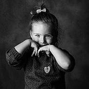 Julia participe au concours pour gagner de l'argent avec cette photo : child, girl, portrait, black_and_white, studio, smile, bow, sweater, hands, eyes, hair, face, young_child, indoor, playful, pose, seated, backdrop, cute, expression