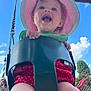 baby, child, swing, playground, outdoor, sunhat, polka_dot, red_clothing, happy, smiling, blue_sky, clouds, greenery, legs, hand, metal_chain, play_equipment, daytime, park, fun