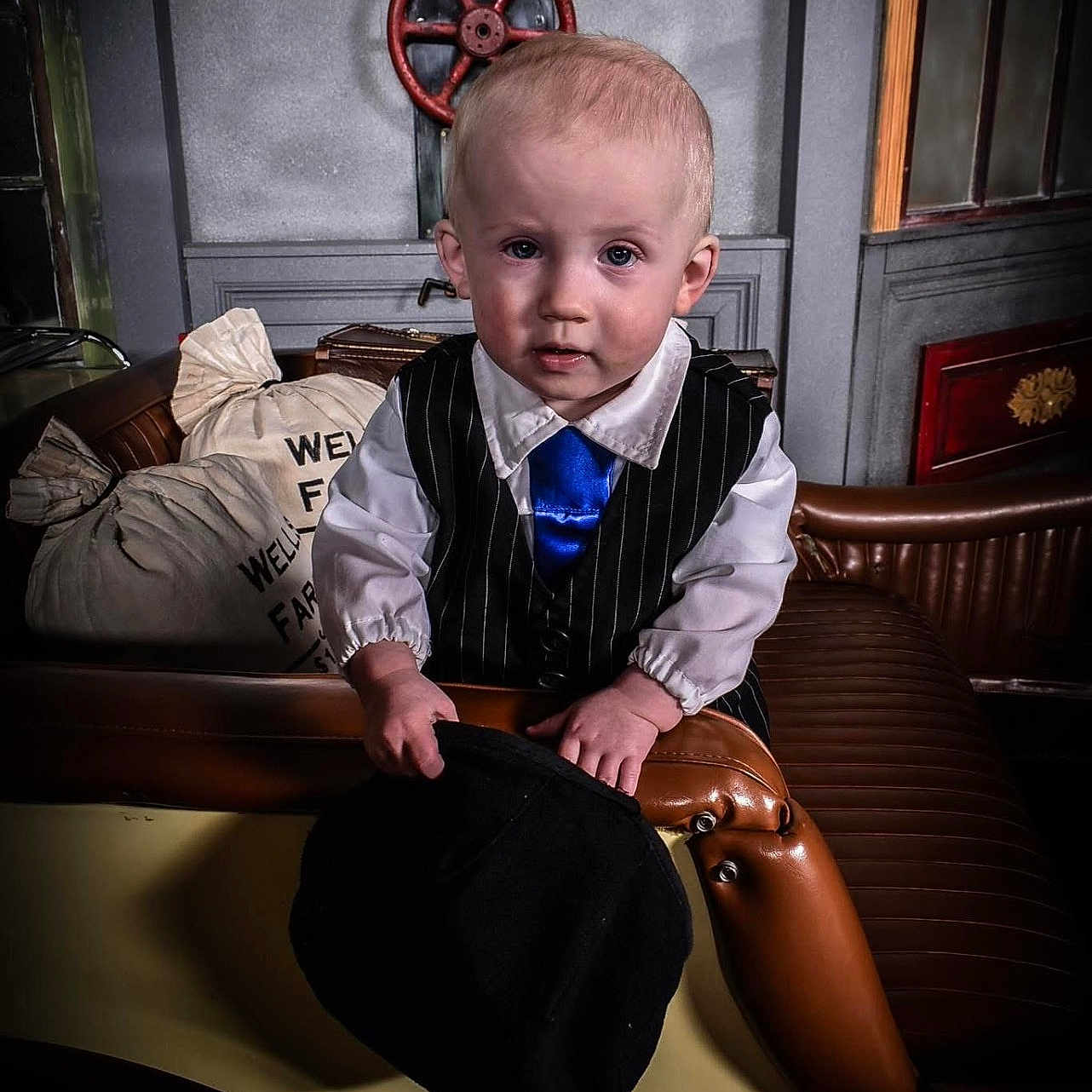 Phoenix is registered to the contest to win money with this photo: baby, blue_tie, boy, child, expression, face, furniture, hand, hat, indoor, industrial, leather_seat, pinstripe, portrait, sack, short_hair, tie, toddler, vest, window