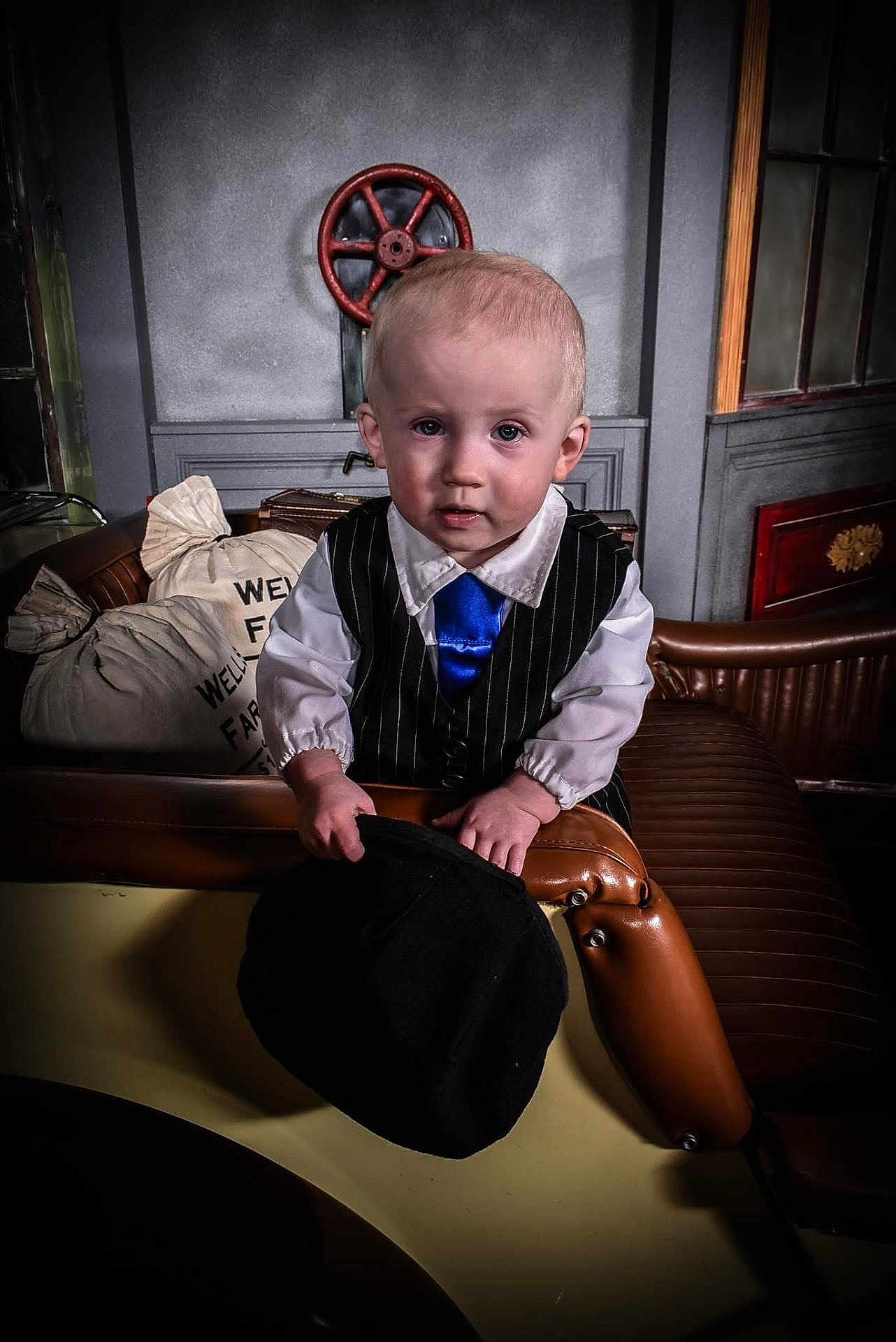 Phoenix is registered to the contest to win money with this photo: toddler, child, boy, vest, tie, hat, leather_seat, indoor, portrait, baby, pinstripe, blue_tie, hand, face, short_hair, sack, industrial, window, furniture, expression