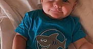 Matthew joined the competition — help win amazing prizes! baby, child, smiling, blue_shirt, shirt_print, bed, bedding, blanket, person, infant, cute, happy, lying_down, human, skin, shorts, indoor, young_child, face, arm
