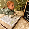 Anthony joined the competition — help win amazing prizes! baby, infant, bible, book, blanket, letter_board, green_clothing, soft_texture, indoors, decorative_plant, wooden_frame, cross, crown, propped_up, curious, portrait, young_child, religious, cozy, toddler