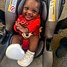 baby, car_seat, car_seat_warning_label, carpet, child, clapping, cute, face, footwear, hair_bow, happy, head, indoor, infant, person, red_clothing, sitting, smiling, toy, white_shoes