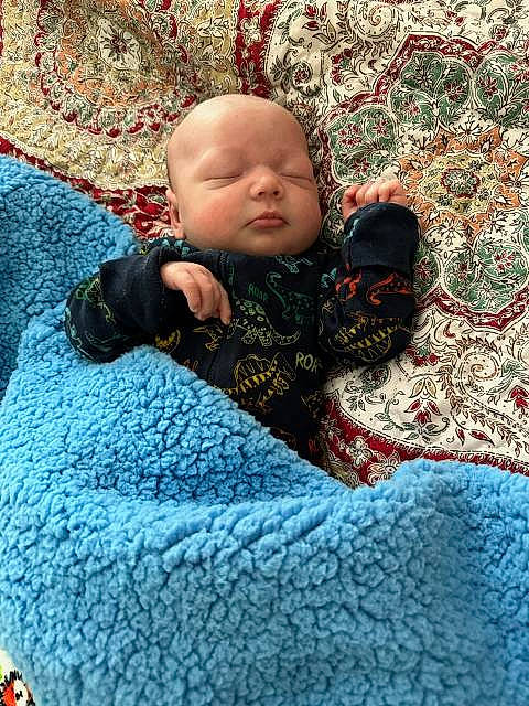 Paxton is registered to the contest to win money with this photo: baby, baby_toddler_clothing, bedding, bedtime, carmine, carpet, cheek, child, comfort, flooring, grass, knitting, linens, nap, pattern, person, room, sitting, textile, toddler