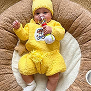 Taimanarii a rejoint le concours — aidez-le/la à gagner de superbes lots ! baby, infant, knitted_hat, yellow_outfit, rattle_toy, hand, face, eyes, socks, plush_bed, round_cushion, blanket, cozy, indoor, wood_floor, knitwear, cute, chubby_cheeks, lying_down, toy