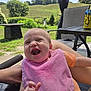 Rose joined the competition — help win amazing prizes! baby, laughing, pink_bib, orange_shirt, outdoor, daylight, greenery, grass, table, chair, person, smile, infant, happy, nature, patio, hand, face, sunlight, relax