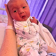 Eddie is registered to the contest to win money with this photo: newborn, baby, infant, onesie, animal_print, hand, arm, purple_curtains, bed, blanket, sleepwear, person, skin, cute, indoors, resting, soft_light, portrait, cozy, small