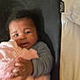 baby, infant, blanket, pink, cushion, black, hand, face, curious, lying_down, indoors, clothing, tag, soft_texture, child, person, closeup, warm, comfort, blur