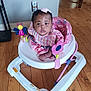 baby, child, walker, pink, toy, floor, wooden_floor, indoor, curious, clothing, person, furniture, seat, playtime, infant, home, cute, smiling, hair_bow, flooring