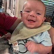 Abbott is registered to the contest to win money with this photo: arm, baby, background, bib, blinds, blue_clothing, clothing, cute, face, hand, happy, holding, home, indoor, infant, person, portrait, red_shirt, smile, window