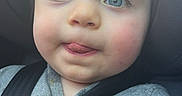 Camron is registered to the contest to win money with this photo: baby, child, car_seat, blue_eyes, tongue_out, seatbelt, safety, close_up, infant, cute, face, person, casual_clothing, indoor, car_interior, warning_sticker, expression, portrait, young_child, seat_harness
