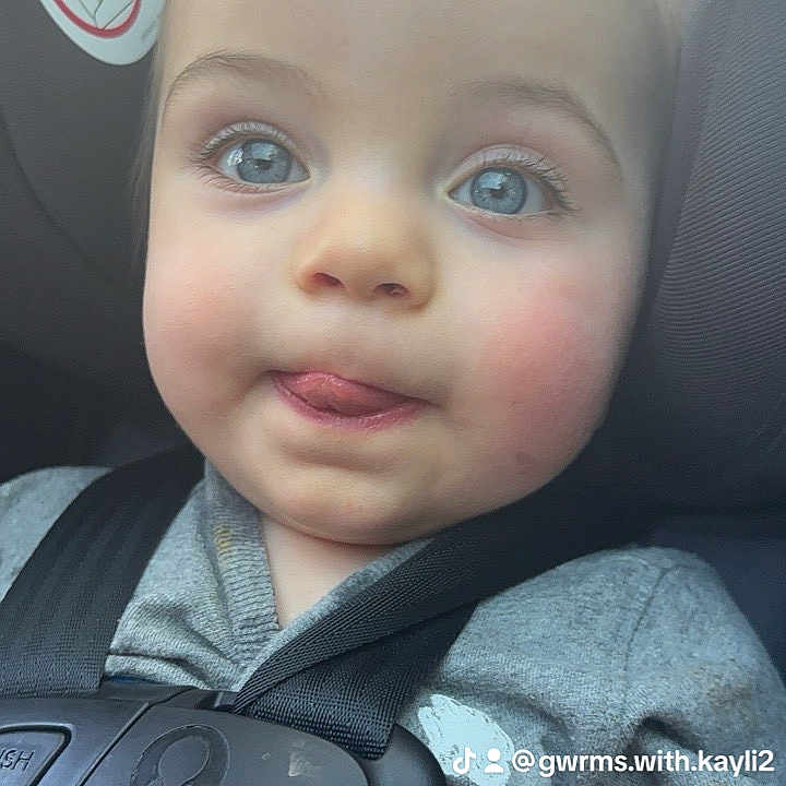 Camron is registered to the contest to win money with this photo: baby, child, car_seat, blue_eyes, tongue_out, seatbelt, safety, close_up, infant, cute, face, person, casual_clothing, indoor, car_interior, warning_sticker, expression, portrait, young_child, seat_harness