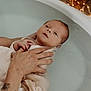 newborn, baby, bathtub, water, blanket, hand, tattoo, infant, bath, skin, relaxation, soothing, wrapped, adult_hand, fairy_lights, warmth, care, gentle, peaceful, indoors