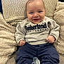 baby, smile, sitting, clothing, sweatshirt, pants, pacifier, couch, plush, white_shoes, happy, indoor, child, face, person, furniture, cozy, cute, young, infant