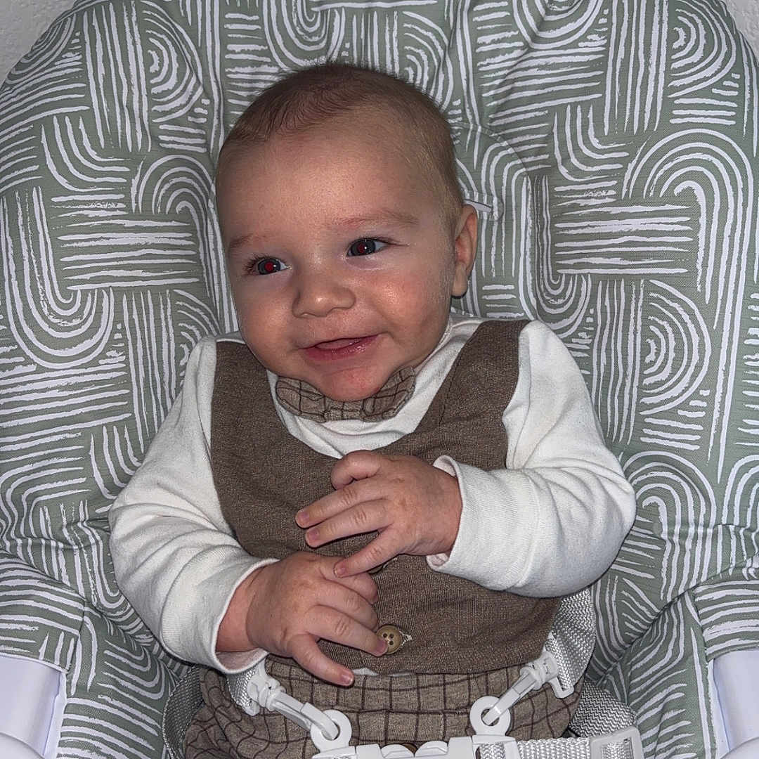 Nëlyo a rejoint le concours — aidez-le/la à gagner de superbes lots ! apparel, baby, brown, child, clothing, cute, fabric, face, hands, happy, high_chair, indoor, infant, patterned, person, safety_belt, seat, smiling, wall, white